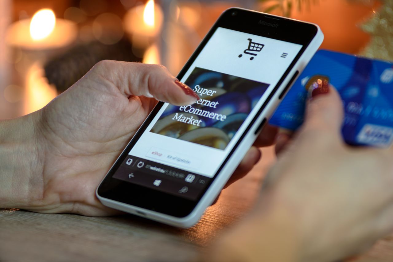 why-choose-us Woman using smartphone for online shopping with credit card in hand, festive background lighting.